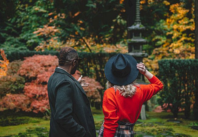 Two people stand among autumn leaves, one adjusting a hat, the scene serene and colorful.