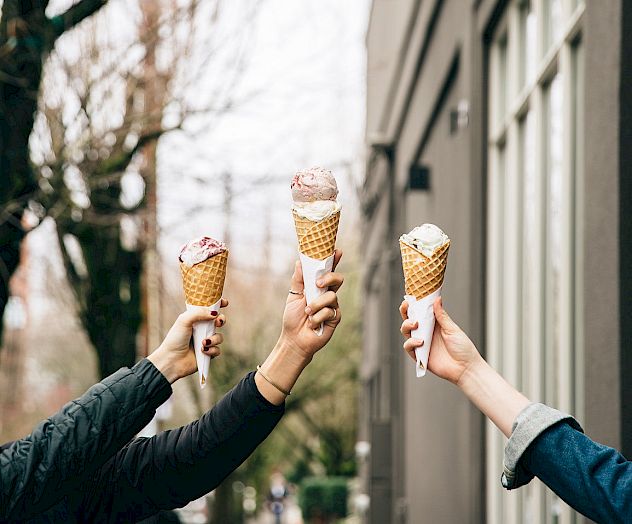 Several hands holding ice cream cones raised beneath a 