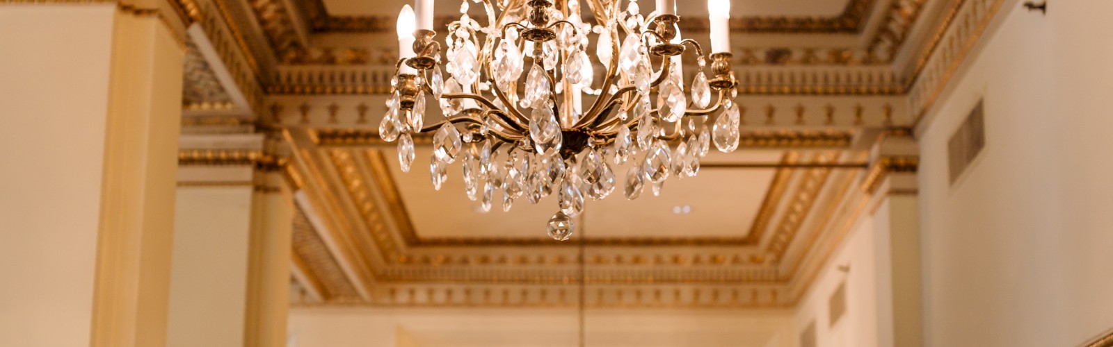 The image shows ornate chandeliers hanging in a luxuriously decorated room with intricate moldings and high ceilings.