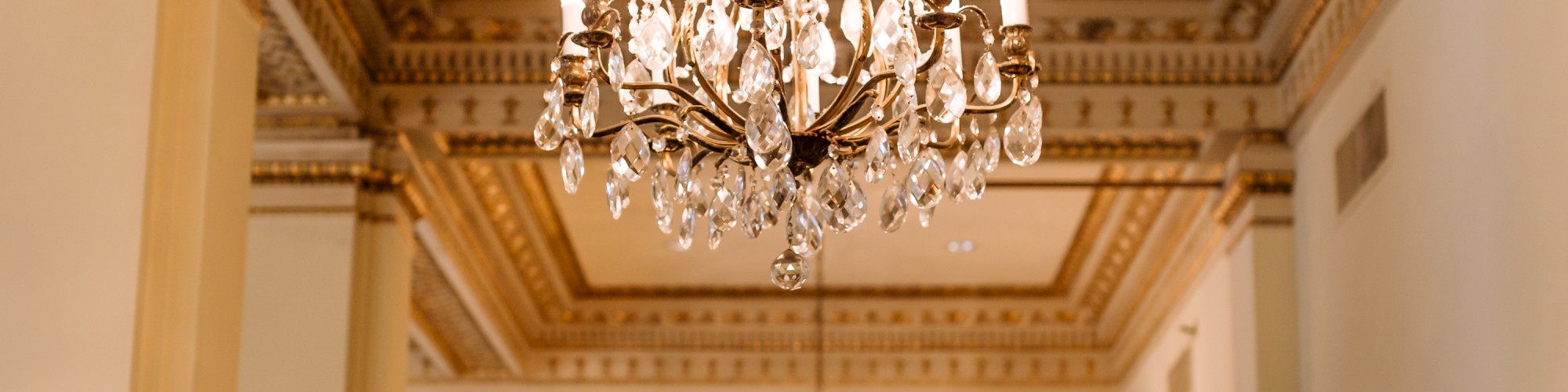 The image shows ornate chandeliers hanging in a luxuriously decorated room with intricate moldings and high ceilings.