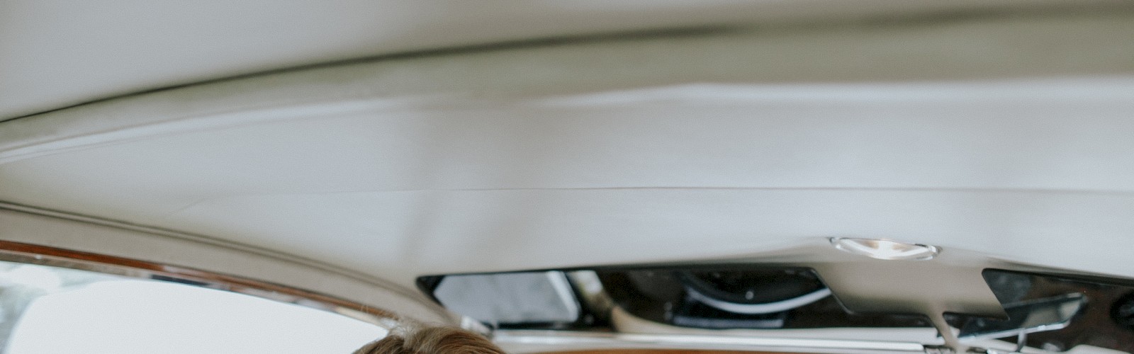 A person wearing sunglasses is sitting in the driver's seat of a vintage car, holding a bouquet of flowers. The car's interior is stylish.