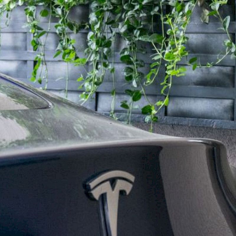 A partial view of a Tesla car charging at a station with a green vertical garden in the background ends the sentence.