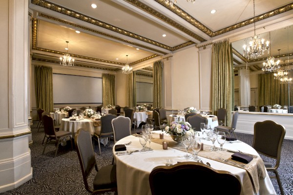 A decorated banquet hall with round tables set for an event, chandelier lighting, mirrors on the walls, and green curtains.