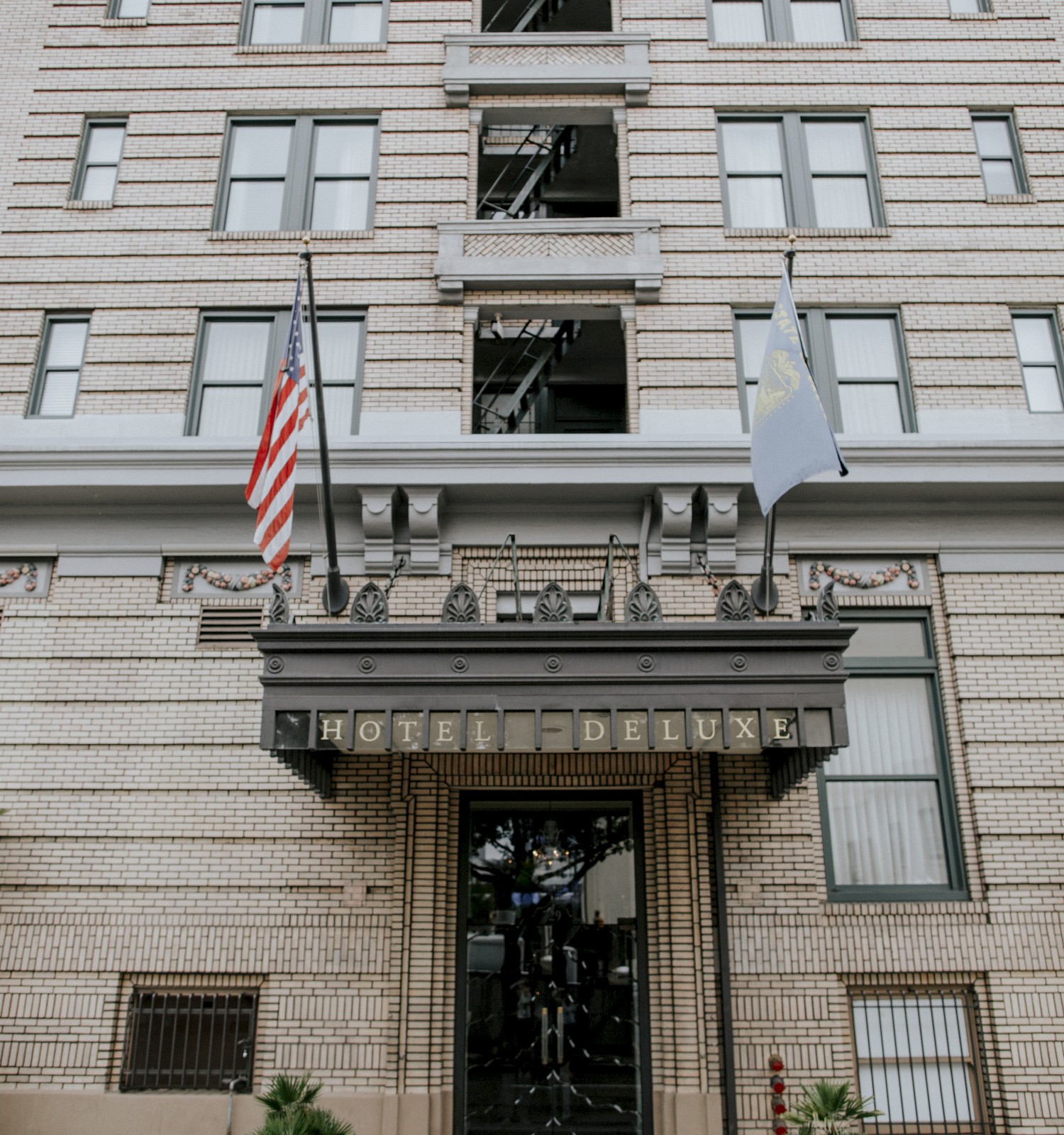 The image shows the entrance of a multi-story building with two flags, one American. Plant pots are on either side of the doorway.