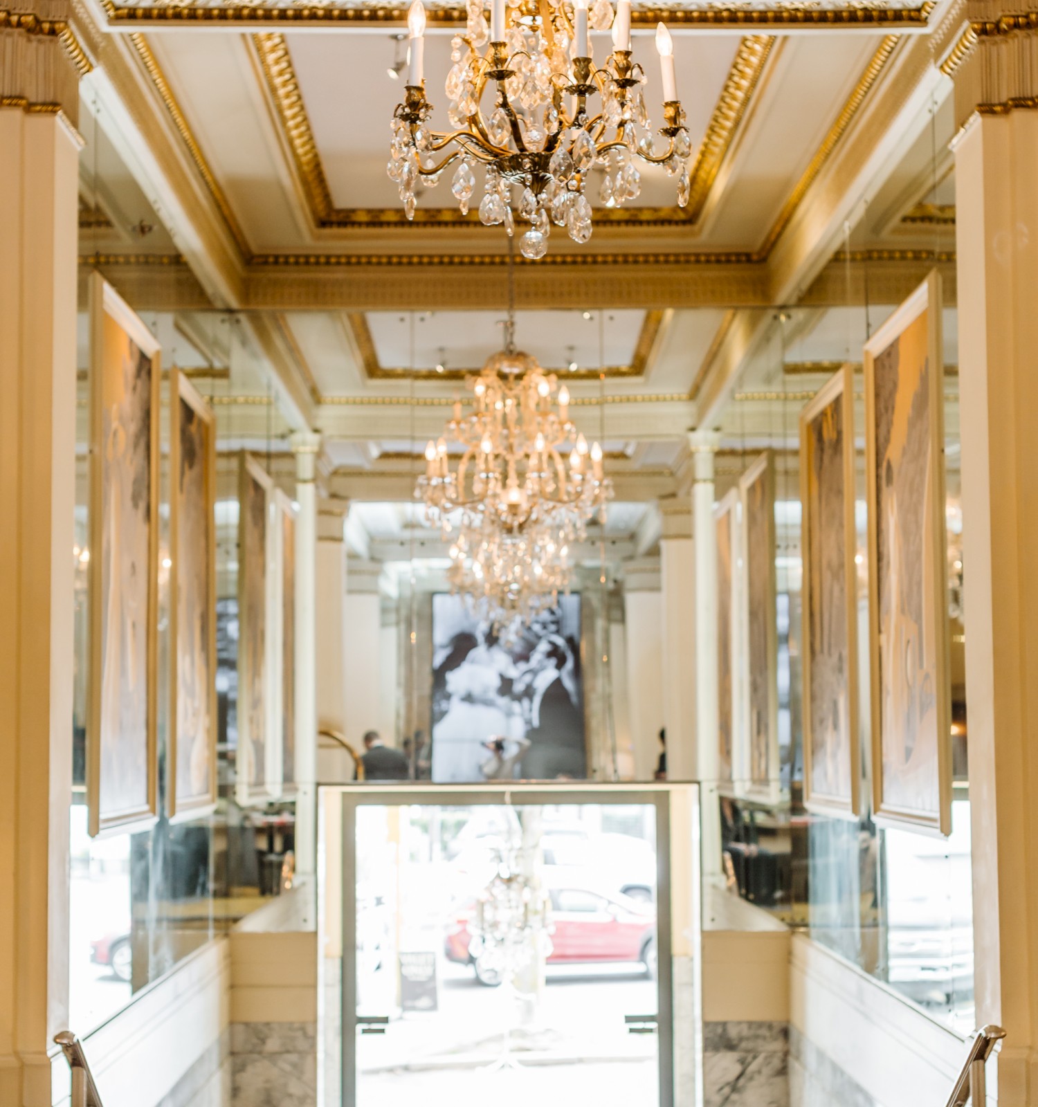 An elegant interior showcases chandeliers, mirrored walls, and marble accents, with a prominently displayed black and white photo emerging beyond the entrance.