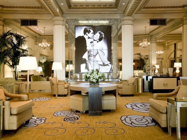 A luxurious lobby with elegant seating, chandeliers, and a large black-and-white photo of a couple kissing on the wall, with floral arrangements.