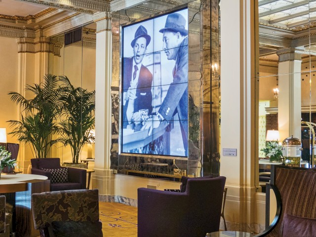 The image shows a luxurious lounge area with elegant decor, comfortable seating, a large photo on the wall, and chandelier lighting.