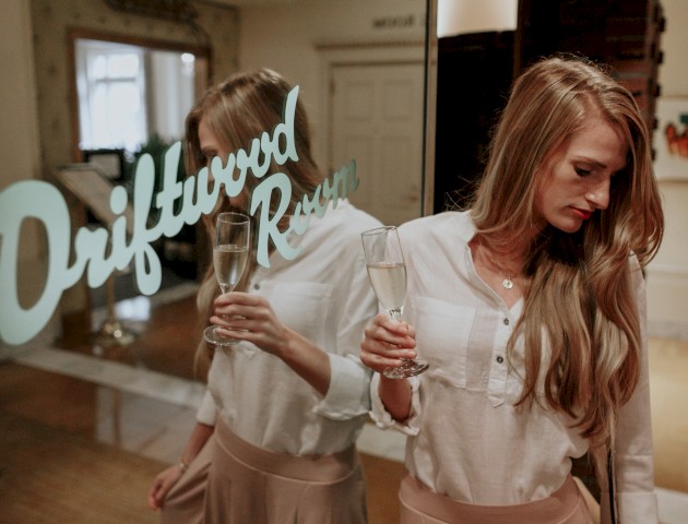 A woman holding a drink stands by a glass door with 