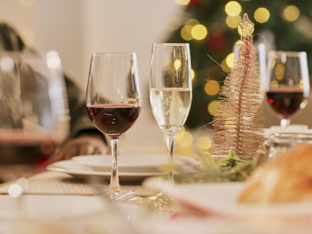 Festive dining setup with wine glasses and a small Christmas tree, blurred lights in the background creating a warm holiday atmosphere.