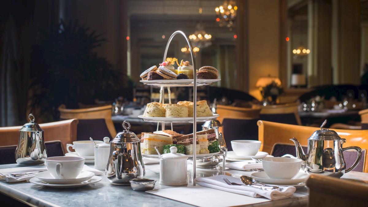 A table set for afternoon tea with a three-tiered stand of pastries and sandwiches, teapots, cups, and saucers elegantly arranged.
