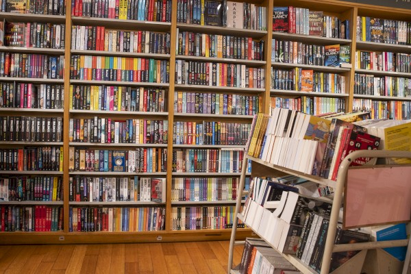 A library scene showing bookshelves filled with books, and a cart with additional books placed in front of the shelves.