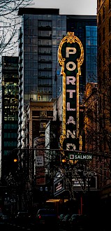 A city street scene at dusk with a prominent colorful vintage sign reading 