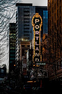 A city street scene at dusk with a prominent colorful vintage sign reading 