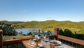 A serene dining setup on a balcony overlooking a lake and hills.