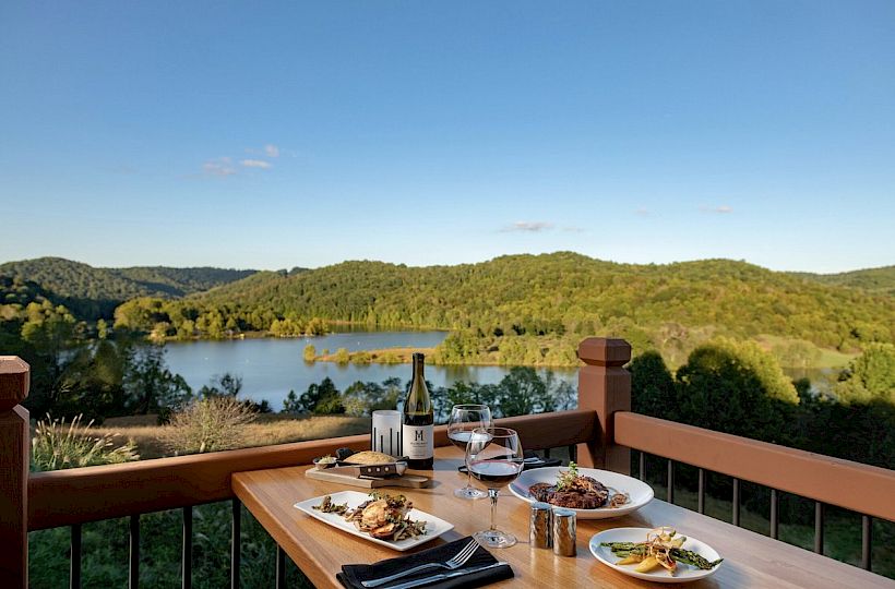 A serene dining setup on a balcony overlooking a lake and hills.
