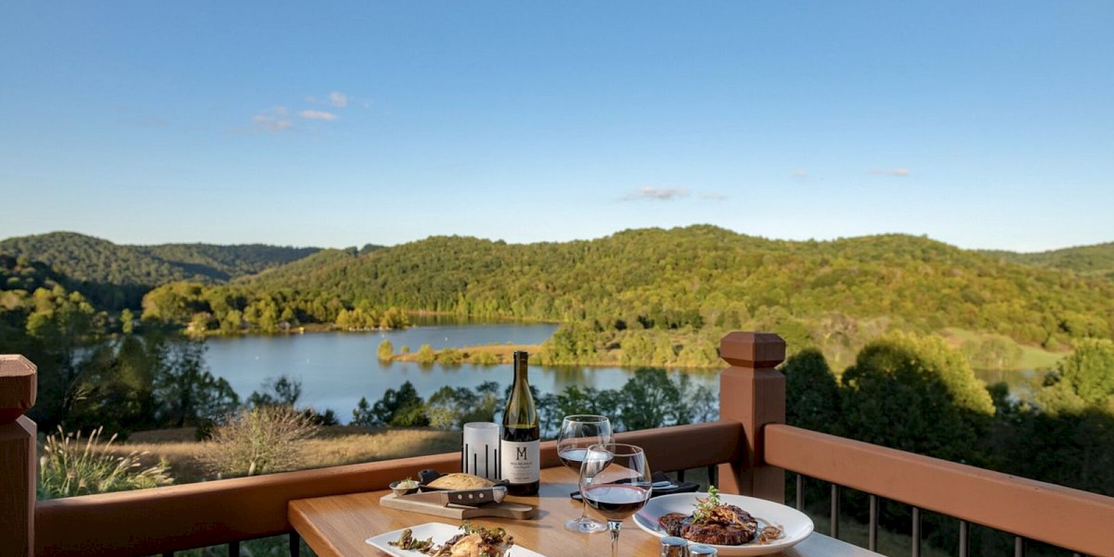 Dining setup on a deck overlooking a scenic lake and hills.
