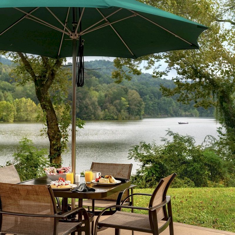 Outdoor dining setup with a lake view, umbrella, chairs, and a laid table.