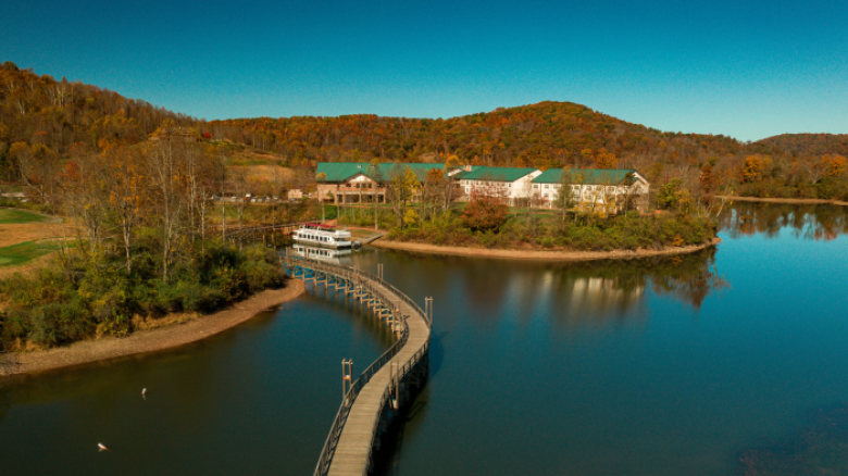 A serene lake with a curved wooden bridge leading to buildings surrounded by autumn trees and hills under a clear blue sky, ending the sentence.